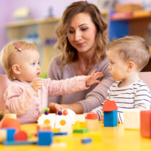 Little girl and boy preschoolers playing with teacher.