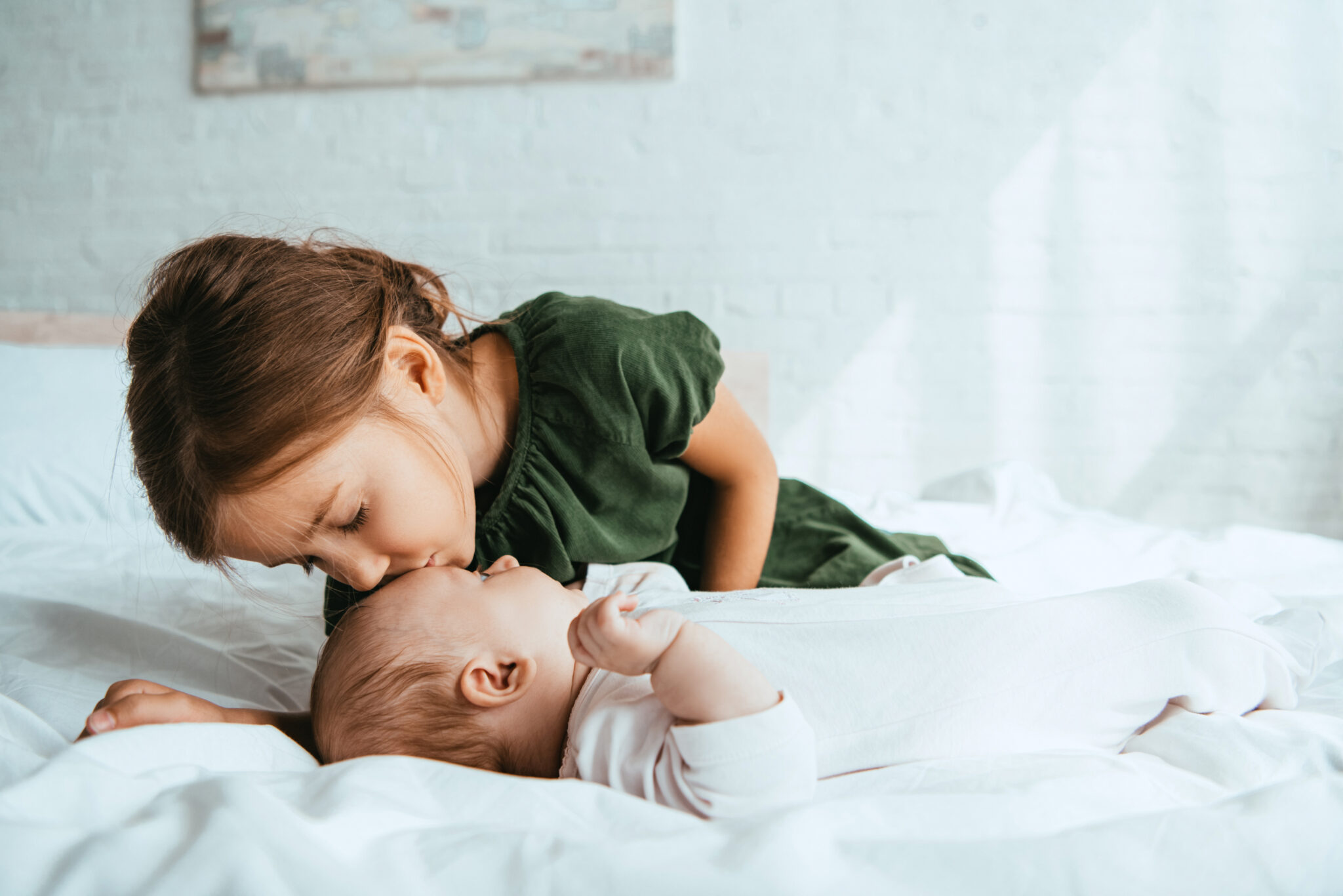 child kissing little sister lying on white bedding