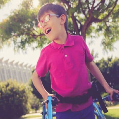 young boy in a garden, smiling, using a walker and wearing a pink t-shirt