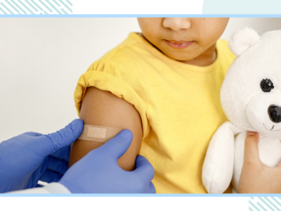 A young child cuddling a teddy has a plaster put on their arm