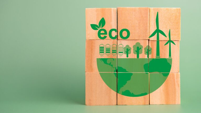 Nine wooden blocks on a green background are stacked in a three by three formation. On the block are green graphics representating the earth trees, wind power and electric. the word eco with a green leaf growing from it is printed on the blocks.