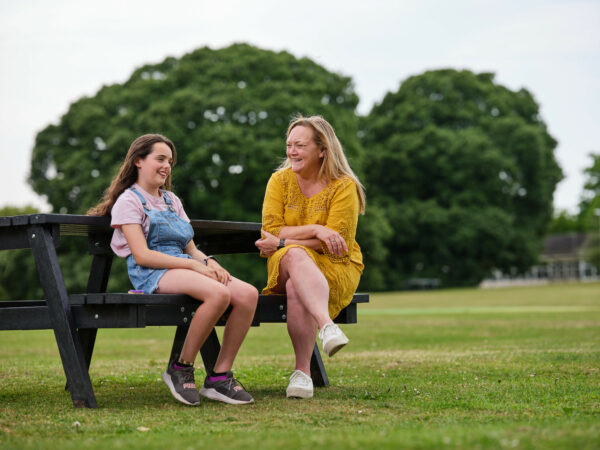 An adult talks to a child while both sat on a park bench.