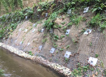 Image of a river bank with metal supports holding the bank back with water running below.