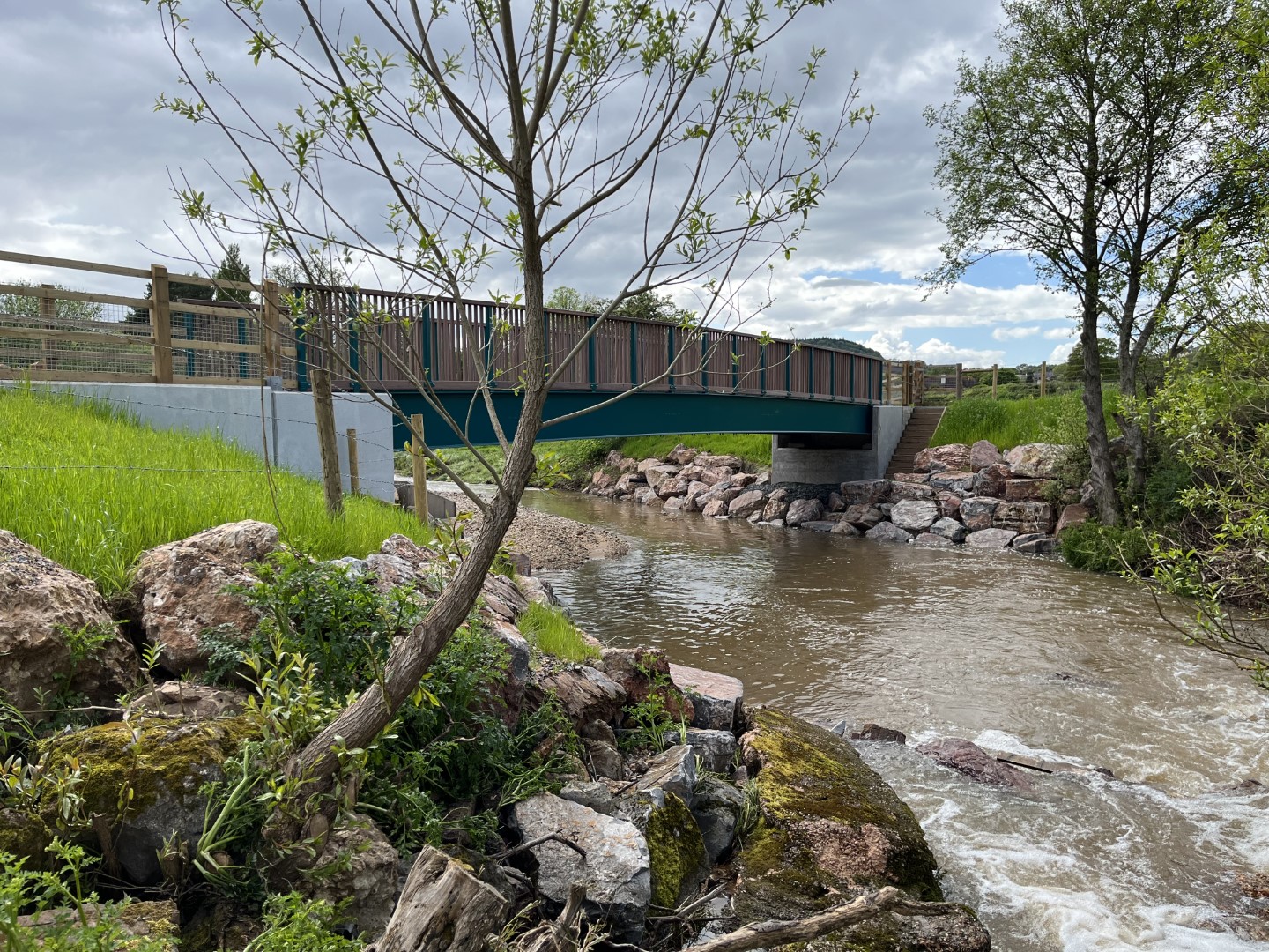Skinners Farm footbridge over a river with rocks and trees in the foreground.